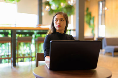 Young woman using phone while sitting on table