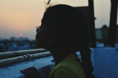 Side view of girl standing by retaining wall at building terrace during sunset