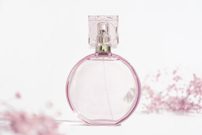 Transparent round pink perfume bottle on white background with small pink flowers