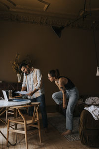 Boyfriend talking on smart phone while standing near non-binary person getting ready at home