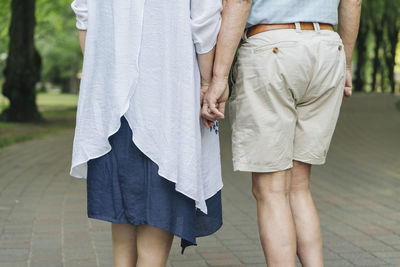 Back view of senior couple holding hands, partial view