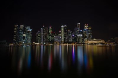 Illuminated cityscape by river against sky at night