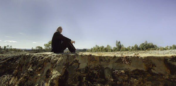 Side view of man sitting on field against blue sky