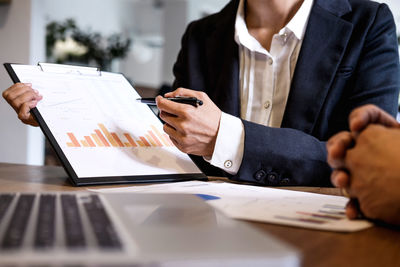 Cropped image of businessman writing on document while colleague sitting table