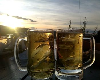 Close-up of beer in glass against sky during sunset