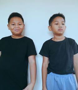 Portrait of smiling boy standing with serious brother against wall