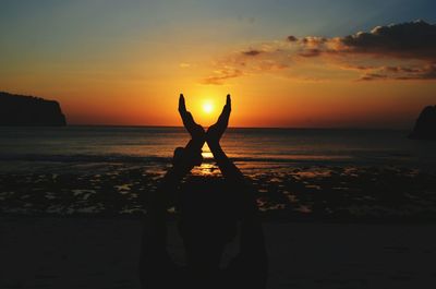 Silhouette woman practicing yoga on beach against sky during sunset