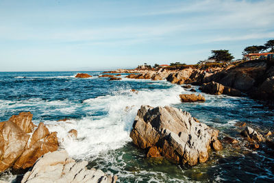 Waves splashing on rocks at shore against sky