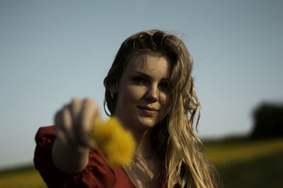 Portrait of woman giving yellow flowers against clear sky