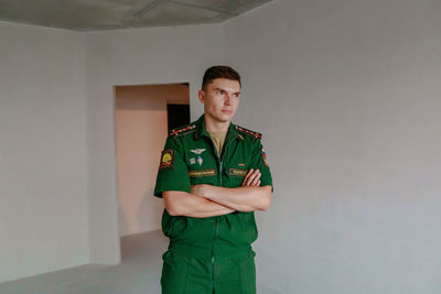 Thoughtful man with arms crossed standing against wall at home