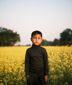 Portrait of young woman standing amidst oilseed rape field against clear sky