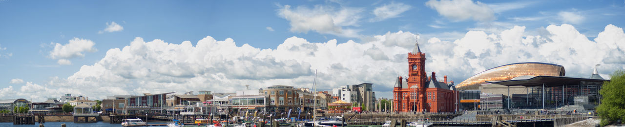 Panoramic view of buildings and church by harbor against cloudy sky