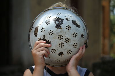 Close-up of boy covering face with colander at home