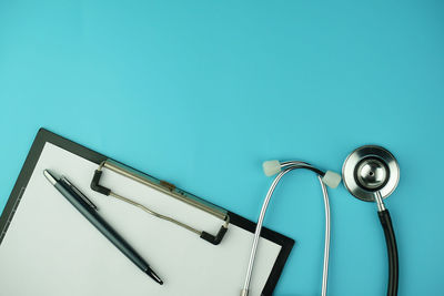 Directly above shot of clipboard and stethoscope on blue background