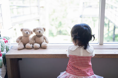 Rear view of girl sitting by window at home