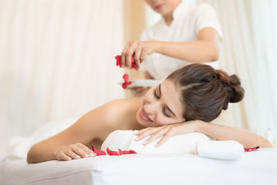 Masseur putting flower petals on young woman in spa