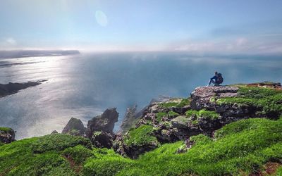 Man standing on cliff by sea against sky