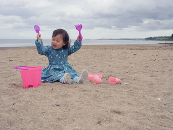Full length of girl playing toys while sitting on sand at beach