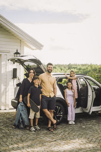 Portrait of happy family standing together outside electric car