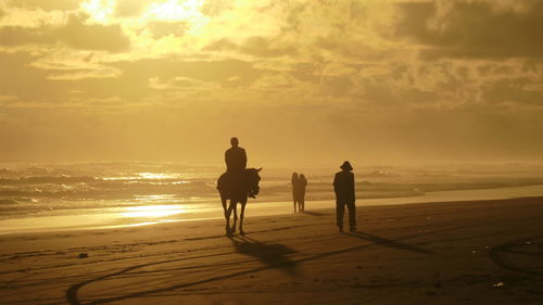 Silhouette people on beach against sky during sunset