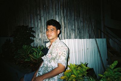 Young man looking away while standing against plants