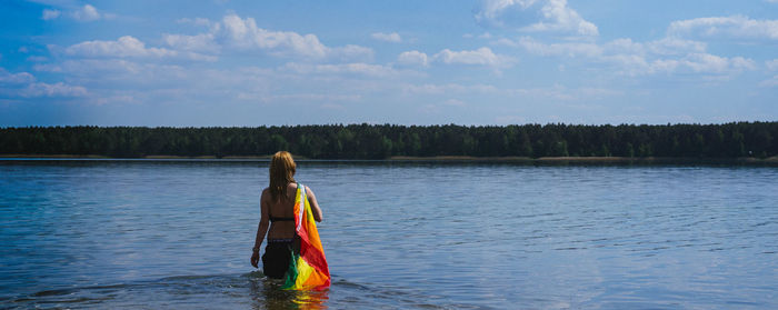 Rear view of woman standing in lake against sky