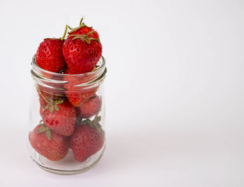 Close-up of strawberries in glass jar against white background