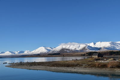 Scenic view of lake and snowcapped mountains against clear blue sky