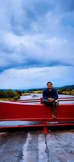 Man sitting on red car against sky