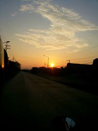 Road by silhouette city against sky during sunset