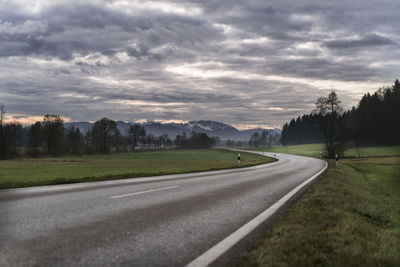 Empty road by landscape against storm clouds