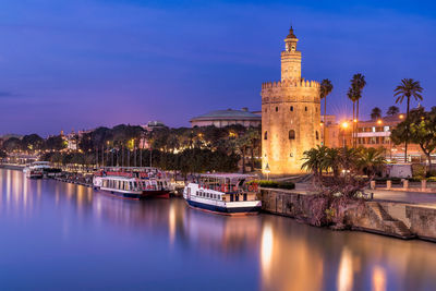 Illuminated buildings by canal against sky at night