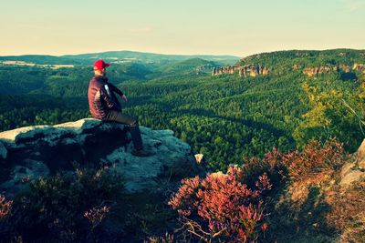 Tall man in black with red baseball cap on sharp cliff and watch to valley. morning in park.