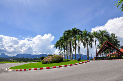 Road by palm trees against sky