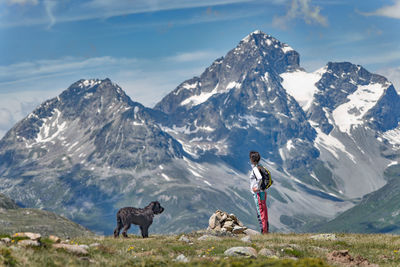 Dog standing on snowcapped mountain against sky