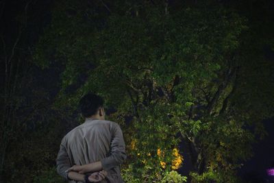 Rear view of man standing against trees at night