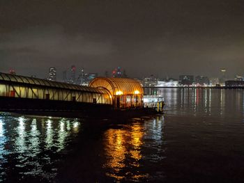 Illuminated buildings by river against sky at night