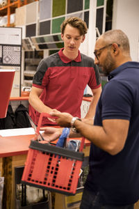 Male cashier talking to mature customer holding basket while standing at checkout in hardware store