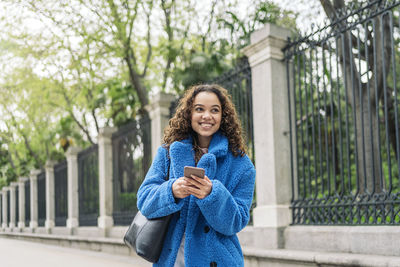 Portrait of smiling young woman using mobile phone at street