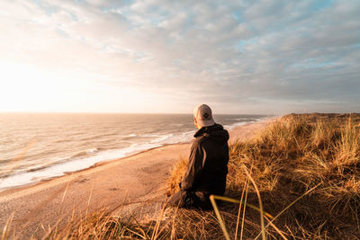 Rear view of woman walking on beach against sky during sunset