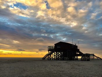 Silhouette lifeguard hut on beach against sky during sunset