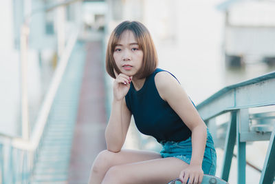 Portrait of young woman sitting against railing