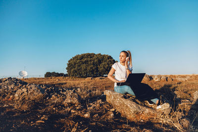 Man sitting on rocks against clear blue sky