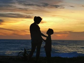 Silhouette friends standing on beach against sky during sunset