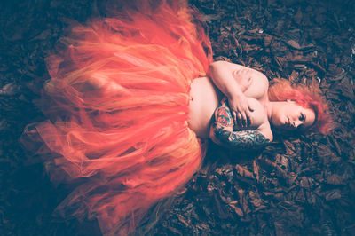 Shirtless woman covering breast with hands while lying down on leaves