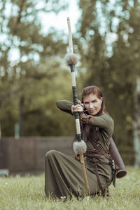 Portrait of archer holding bow and arrow crouching on field