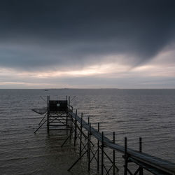 Pier over sea against cloudy sky at dusk