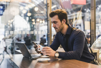 Young businessman in a cafe at train station with cell phone and laptop