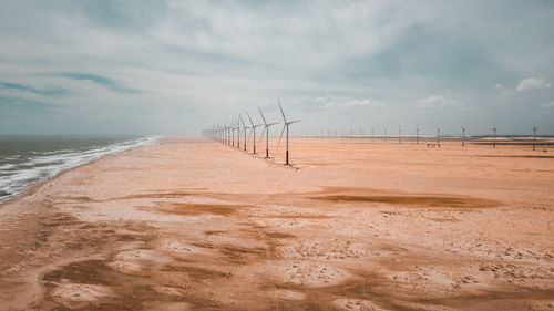 Windmills at beach against cloudy sky