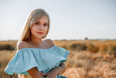 Close-up portrait of teenage girl wearing dress standing on land against sky